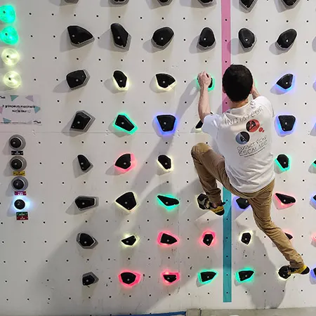 Grimpeur touchant une prise illuminée pendant une partie sur le mur de jeu Luxov à Vichy
